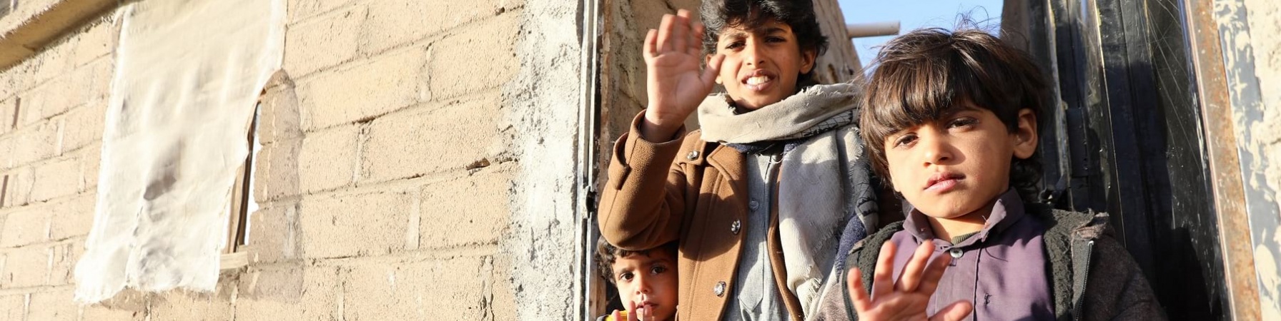 Tre bambini yemeniti in piedi tra due edifici mostrano la mano aperta a cinque