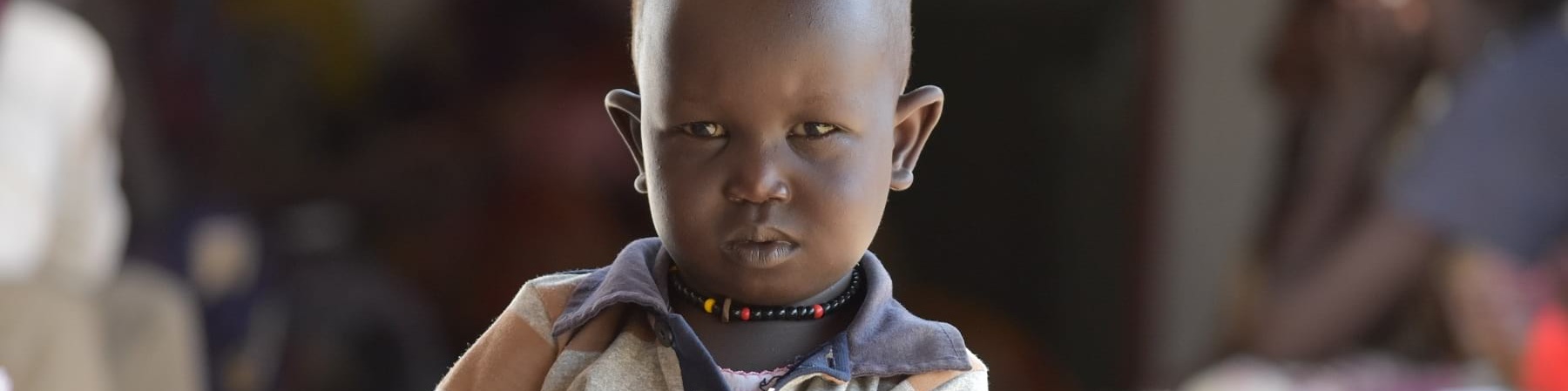 Mezzo busto di un bambino sudanese con maglietta a righe arancioni blu e bianche che tiene con due mani un foglio