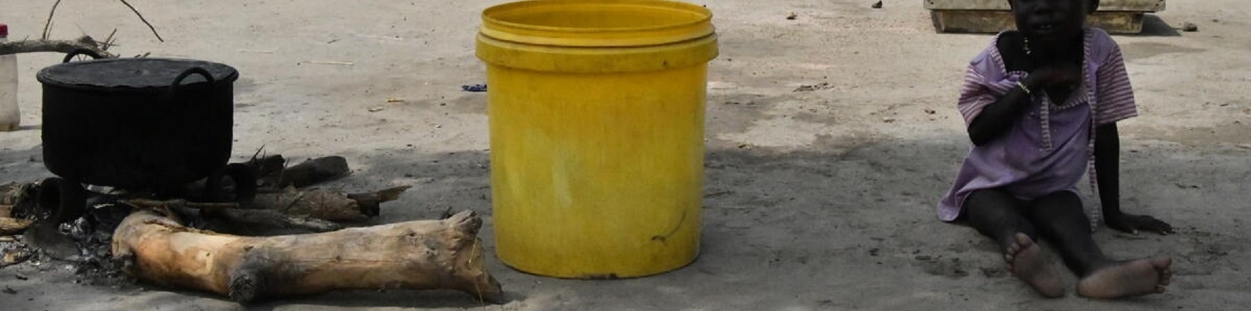 bambino seduto a terra accanto secchio giallo acqua