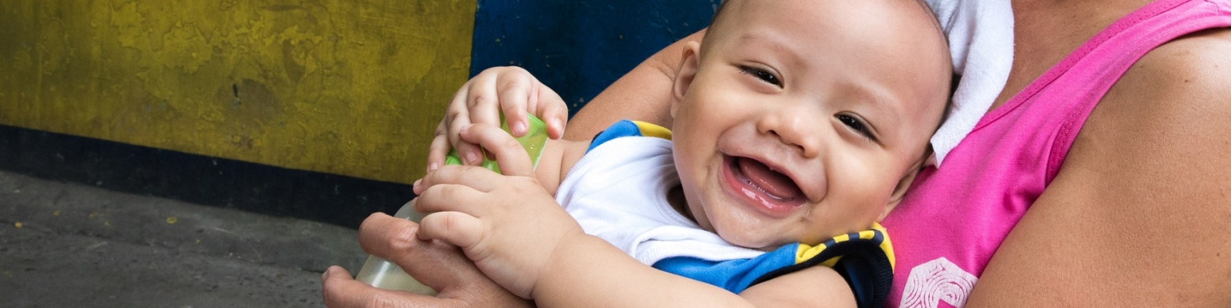 bambino sorridente con biberon e braccia della mamma