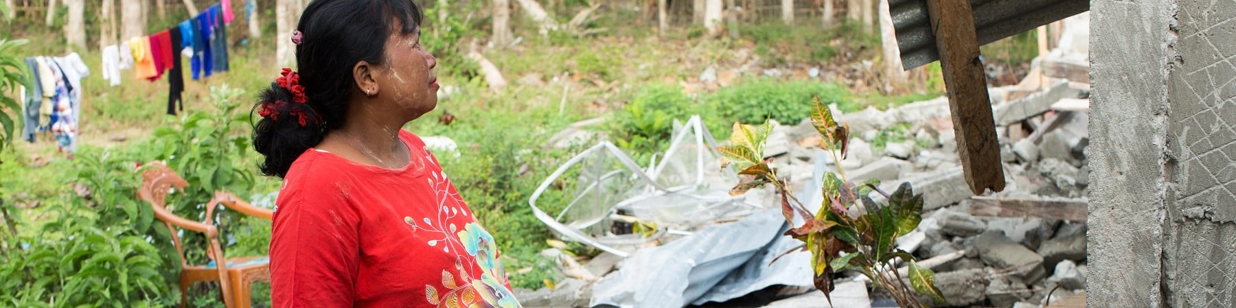 Donna indonesiana in cinta sta in piedi di profilo e guarda di fronte a lei un abitazione distrutta dal terremoto