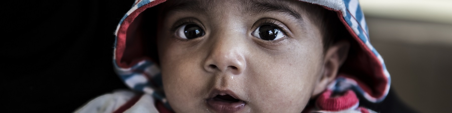 bambino di pochi mesi inquadrato in primo piano con tutina e cappuccio sulla testa