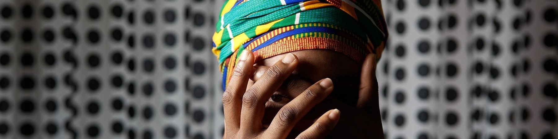 ragazza con foulard colorato in testa che si copre il volto con le mani 