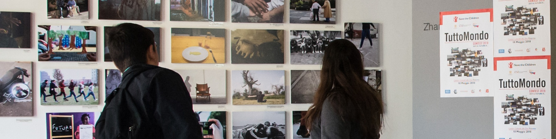 due ragazzi in un museo, in piedi, di spalle, guardano delle fotografie appese a un muro