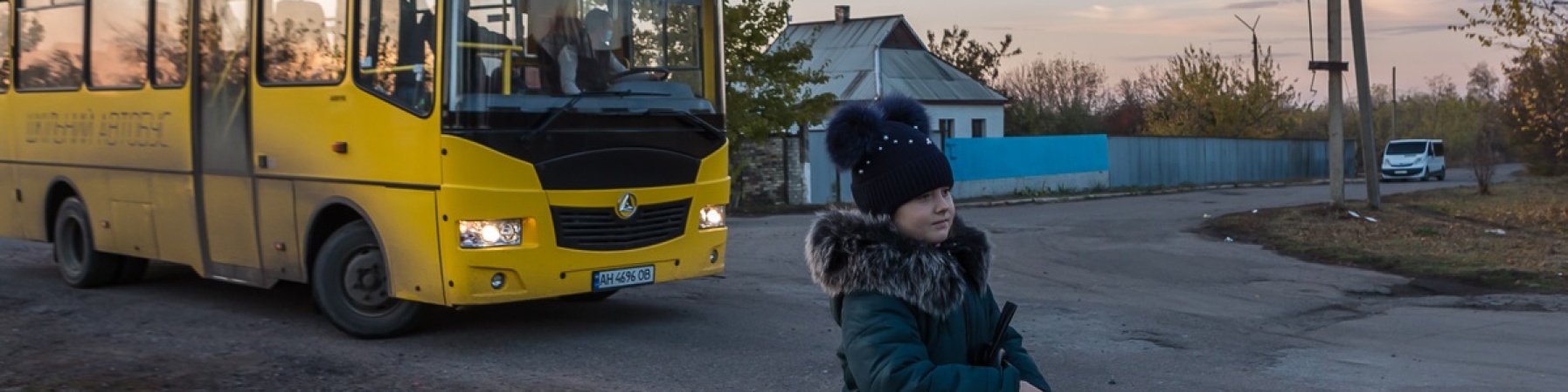 bambina cammina di fronte ad uno scuola bus giallo in Ucraina