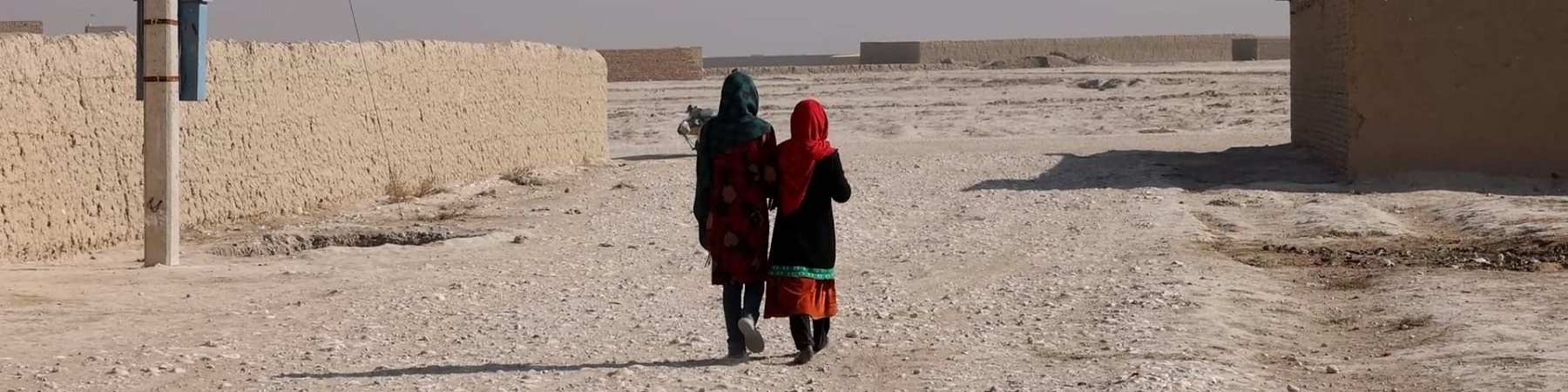 due bambine afghane riprese mentre camminano di spalle in territorio desertico