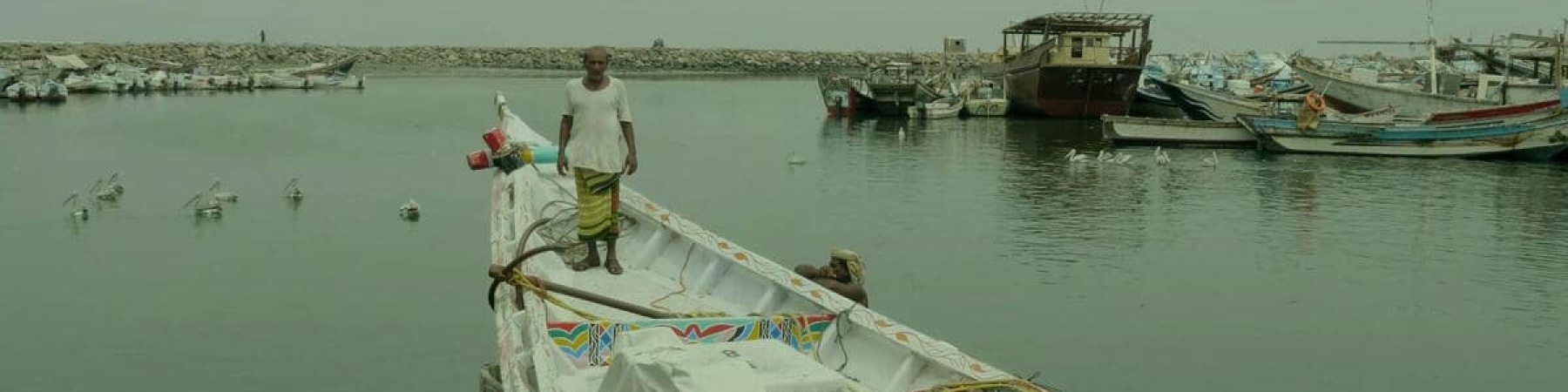 pescatore con maglia bianca in piedi sulla prua di una barca bianca ormeggiata al porto in Yemen