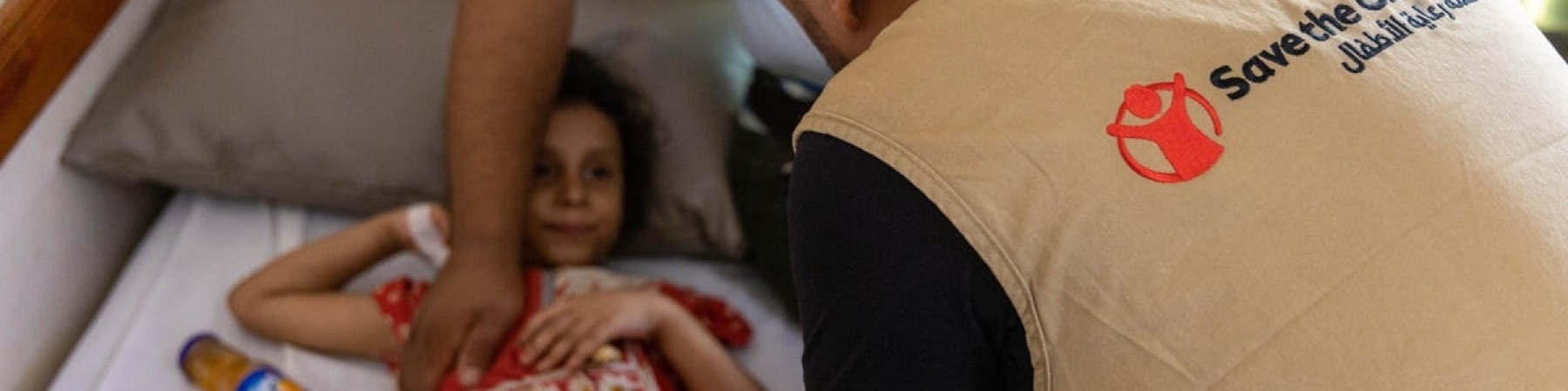 bambina colpita da un bombardamento in yemen su un letto di una nostra clinica con accanto un operatore save the children