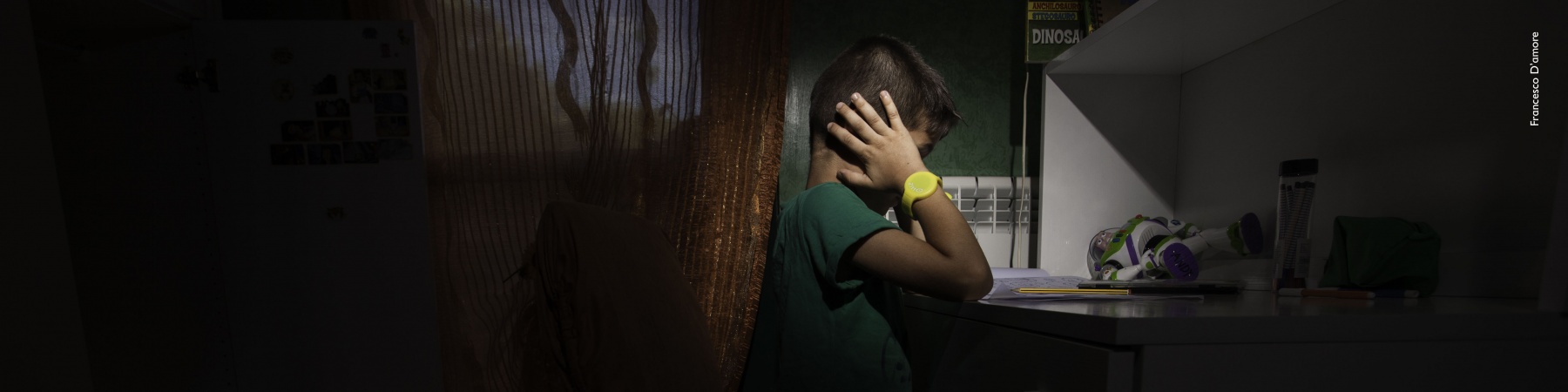 Bambino nella sua stanza buia si copre le orecchie con le mani