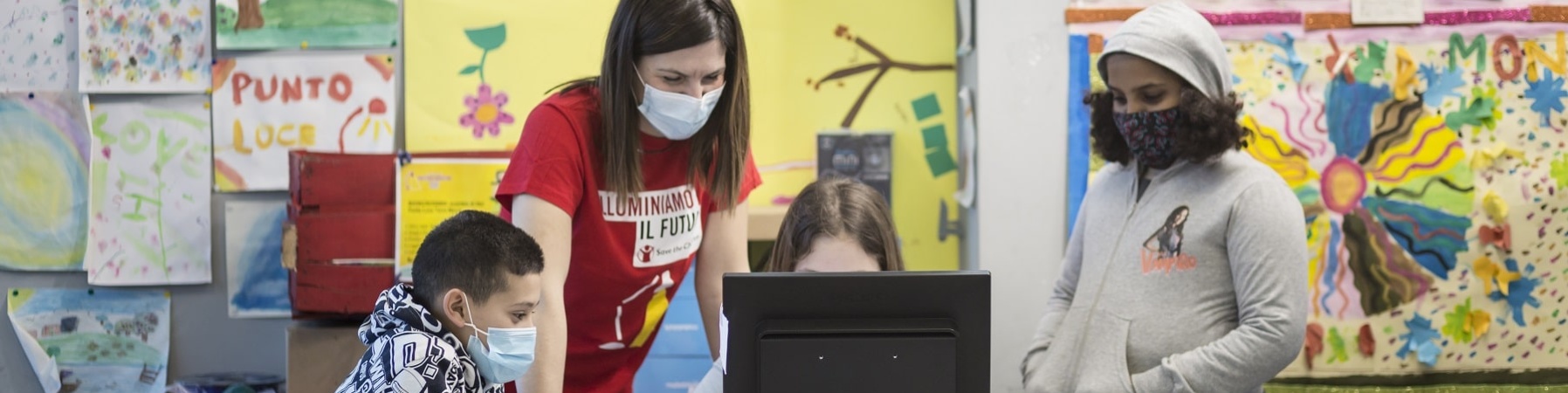 un ragazzo e due ragazze con un operatrice Save the Children studiano davanti a un PC