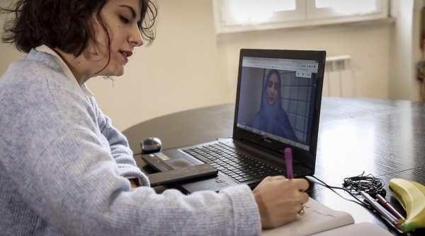 volontaria di Save the Children Italia con maglioncino grigio davanti al PC in videochiamata con dei ragazzi