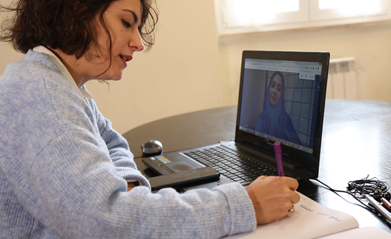 volontaria di Save the Children Italia con maglioncino grigio davanti al PC in videochiamata con dei ragazzi