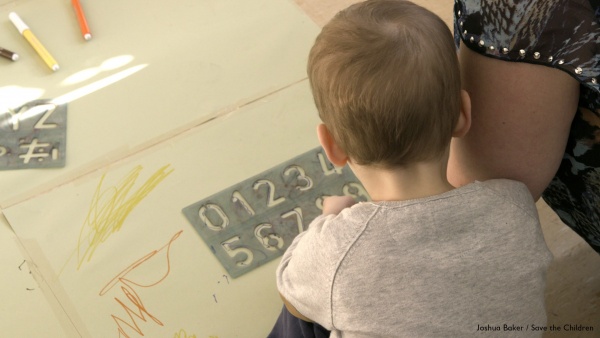 bambino al banco disegna con pastelli colorati su un foglio bianco
