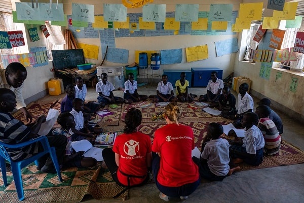 Un gruppo di bambine e bambini studia in cerchio assieme a due operatori di Save the Children