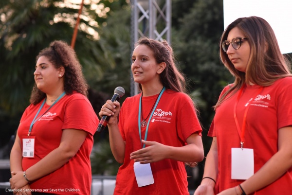 tre ragazze su un palkco con maglietta rossa del movimento giovani sottosopra save the childrten Italia