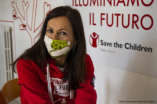 operatrice di Save the Children con la mascherina civile seduta nel centro Illuminiamo il futuro che guarda in camera