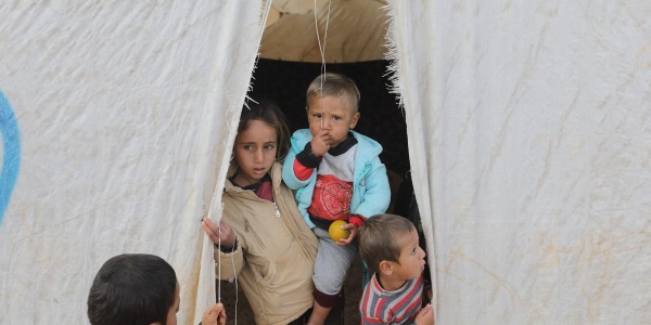 quattro bambini siriani sono sulla soglia di una tenda di un campo rifugiati, una di loro è più grande e tiene in braccio un altro.