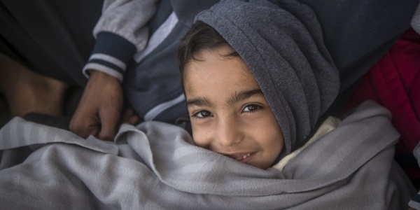 Un bambino con cappuccio grigio in testa sorride avvolto in una coperta anche essa grigia.