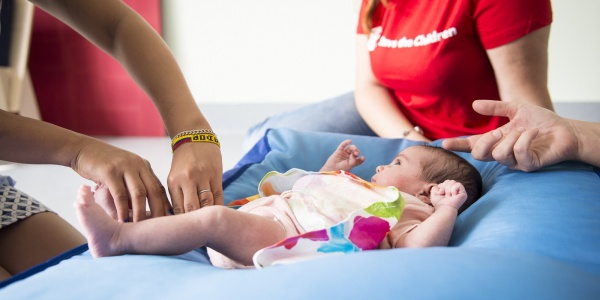 3 operatrici save the children Italia al fianco di un neonato sdraiato su un cuscino blu