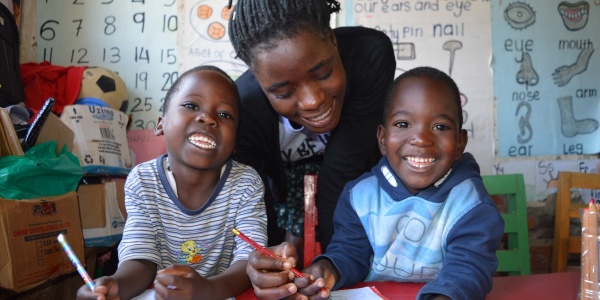 2 bimbi neri con la maestra studiano sorridenti seduti al banco di scuola