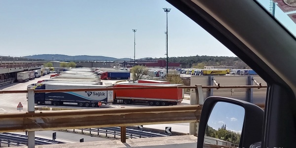 piazzale di camion ripreso dal finestrino di una macchina della quale si vede anche uno specchietto.