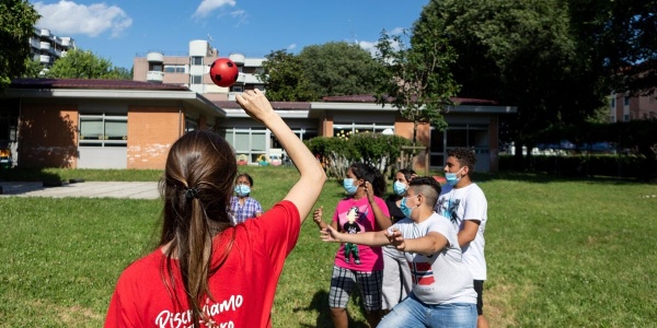 Un operatrice Save the children di spalle gioca a palla con bambini su un prato