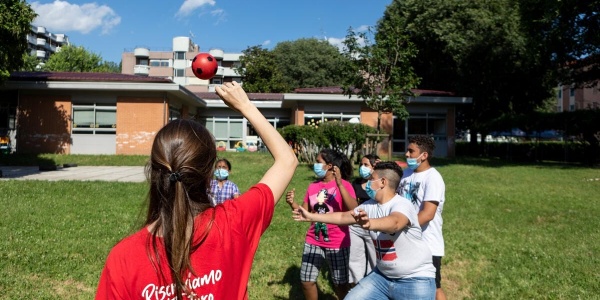 Un operatrice Save the children di spalle gioca a palla con bambini su un prato