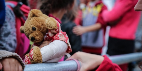 le mani di due bambini afferrano lastra di acciaio accanto a peluche in primo piano