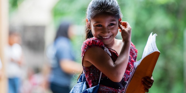 bambina di el Salvador sorridente con una borsa a tracolla e un libro in mano