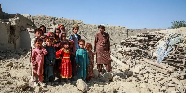 Bambine e bambini con accanto uno zio in mezzo ai detriti della loro casa distrutta dal terremoto in Afghanistan
