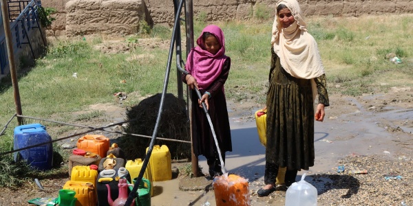 Due bambine afghane prendono acqua da una pompa in mezzo a un campo brullo