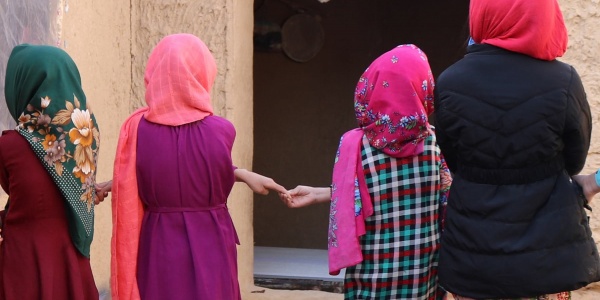 4 bambine afghane di spalle si tengono per mano, indossano chador e vestiti colorati