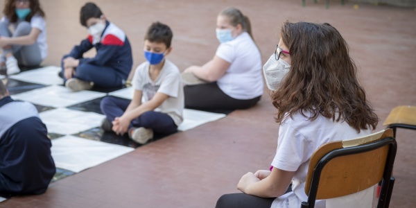 ragazza seduta su una sedia di scuola indossa mascherina e guarda i compagni davanti a lei seduti per terra