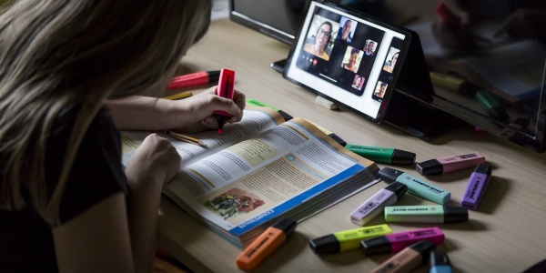 Bambina di spalle evidenzia libro scolastica mentre fa lezione a distanza su un tablet davanti a lei