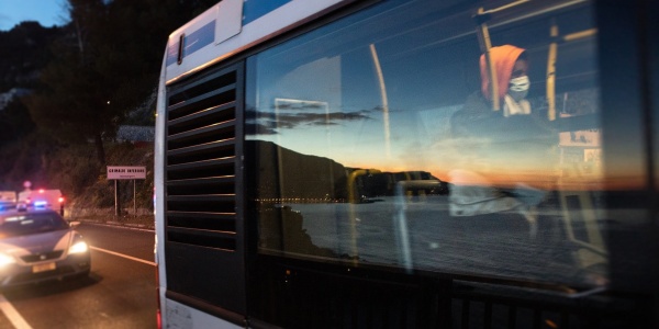 Finestrino di un autobus con riflesso il mare e i colori del tramonto, all'interno di vede un ragazzo seduto 