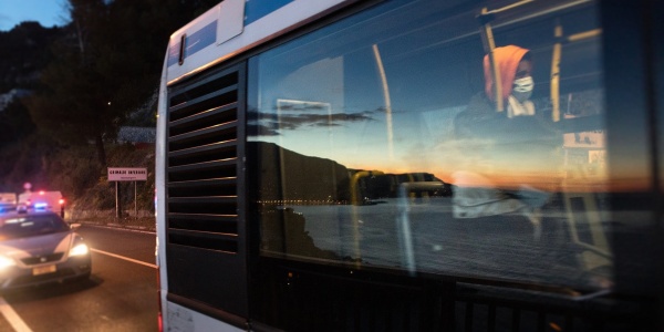 Finestrino di un autobus con riflesso il mare e i colori del tramonto, all'interno di vede un ragazzo seduto