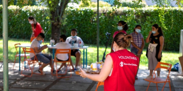 Volontaria in primo piano con un vassoio con sopra la merenda per i ragazzi sullo sfondo del centro Arcipelago educativo