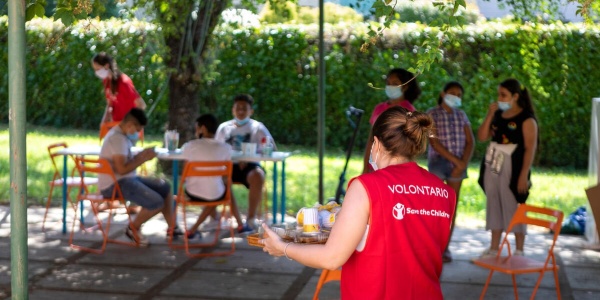 Volontaria in primo piano con un vassoio con sopra la merenda per i ragazzi sullo sfondo del centro Arcipelago educativo 