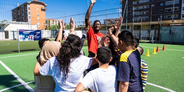 bambini e bambine in campetto da calcio riuniti in cerchio per giocare con operatore Save the Children