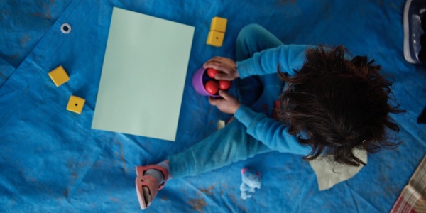 foto dall alto di bimba seduta per terra mentre gioca con delle palline rosse