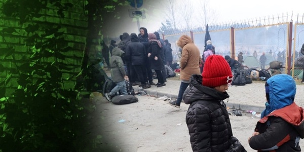 due bambini seduti su un tubo, vestiti invernali. Sullo sfondo altre persone. Sono tutti migranti bloccati al confine con l'Europa. A sinistra della foto una finestra con lue verde simbolo di speranza.