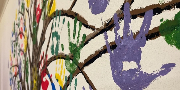 impronte mani colorate di bambini dipinte su muro attorno a rami 