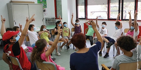 classe di bambini seduti in cerchio con le mani alzate 