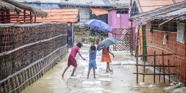 Tre bambini di spalle reggono ombrello e giocano in uno slum allagata del Bangladesh