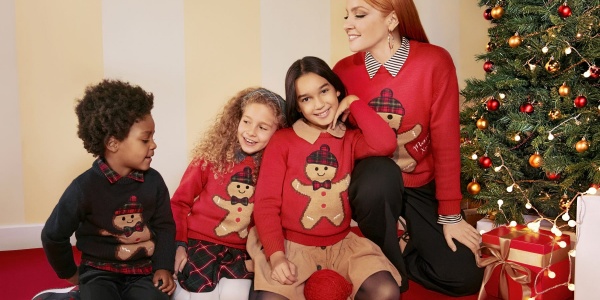 La cantante Noemi insieme ad alcuni bambini indossa il Xmas Jumper di OVS vicino a un albero Natale