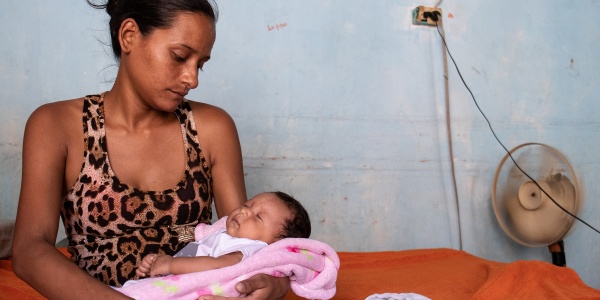 Donna venezuelana seduta su un letto tiene in braccio e guarda il figlio neonato.