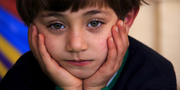 primo piano bambino imbronciato con la testa appoggiata tra le mani. Capelli a caschetto e maglioncino nero con righe bianche e verdi sui polsi.