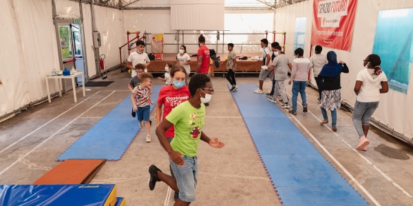 Bambini che corrono in cerchio in una palestra. A terra materassini azzurri