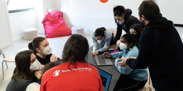 ragazzi e ragazze guidate da operatore save the children mentre lavorano in gruppo al computer