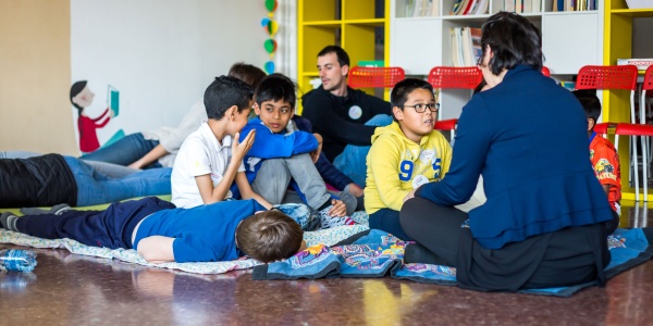 bambini seduti a terra che giocano insieme ad un insegnante dopo il rientro a scuola